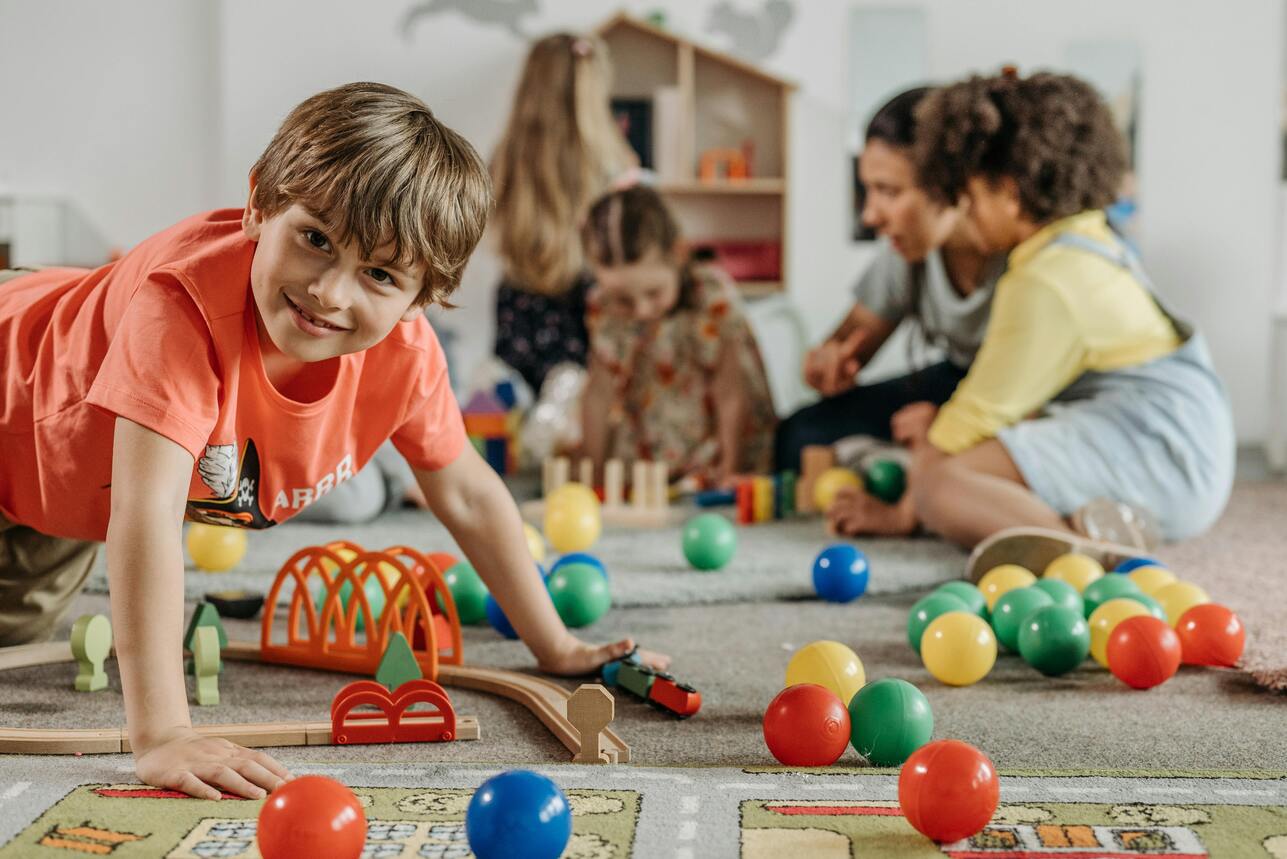 Children playing with colorful toys and wooden train tracks on a carpet, focused boy in orange shirt