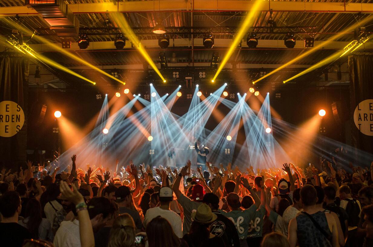 Group of people cheering at a sunny Nashville music festival with band playing on stage and colorful crowd