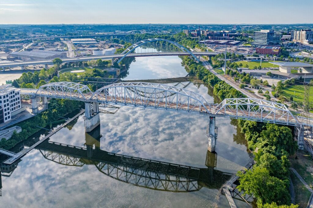 Aerial view of multiple bridges crossing a river with city buildings, greenery along shorelines, and cloud reflections in water