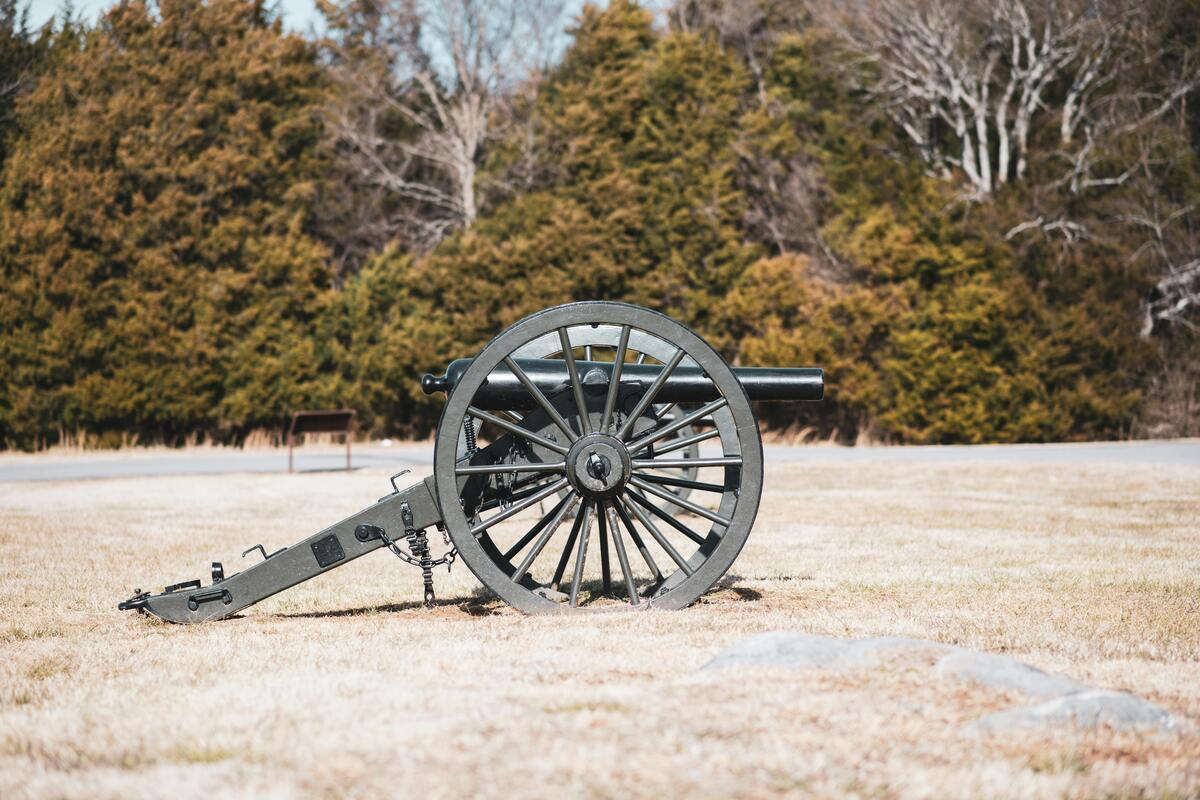 Historic cannon artillery piece displayed on grassy fort field with evergreen and bare trees in background