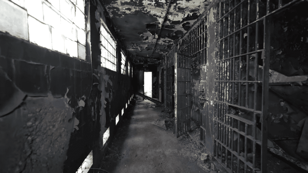 Deteriorating corridor inside abandoned Old Tennessee State Prison showing cell bars, broken windows and decaying ceiling