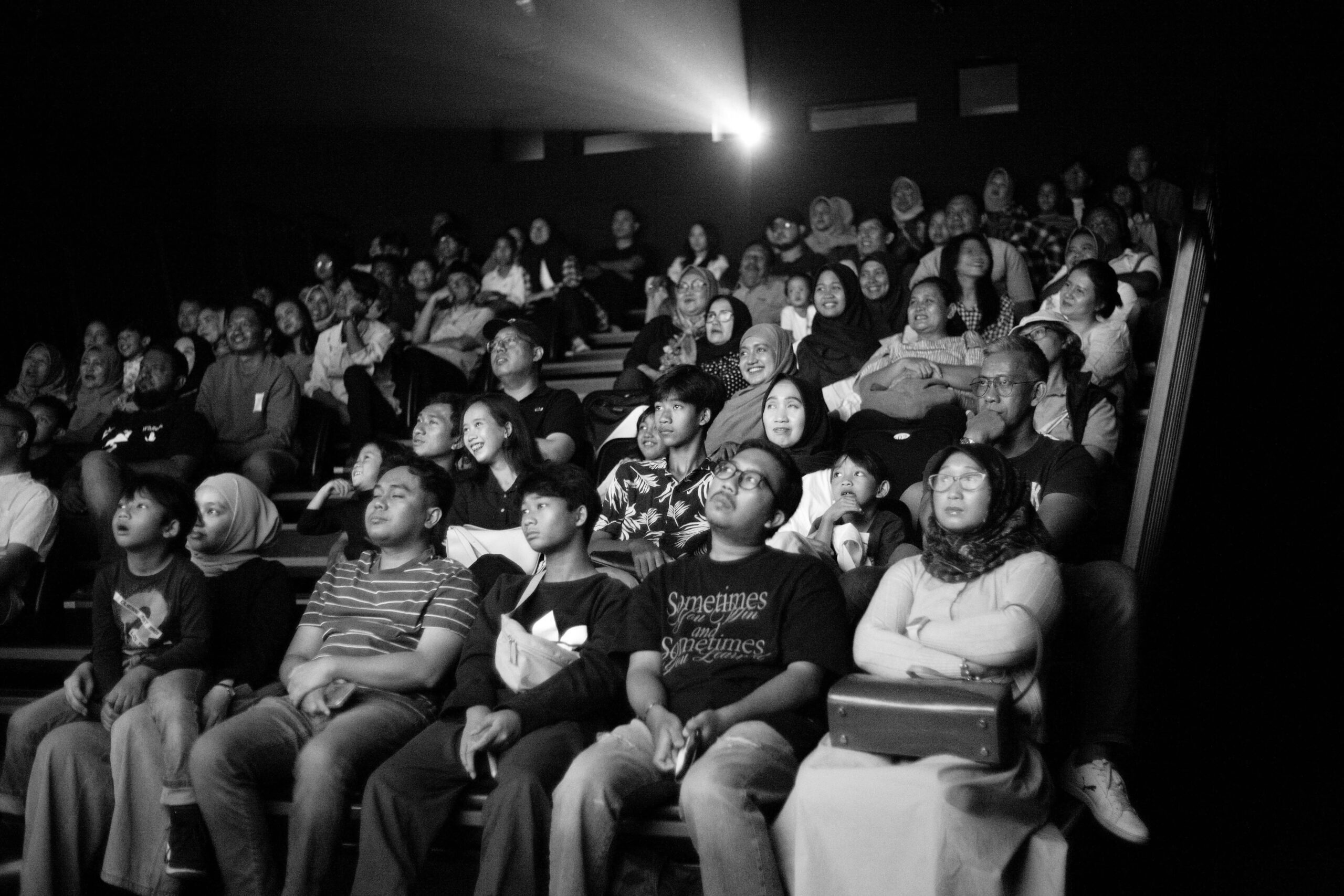 Black and white photo: a captivated theater audience, bathed in dramatic lighting, lost in the performance