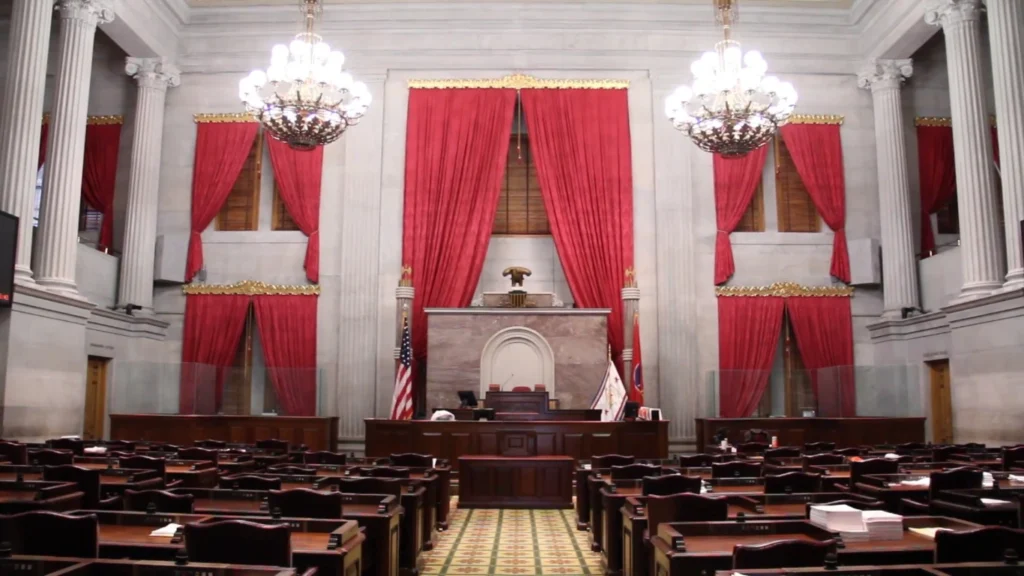 Tennessee State Capitol House chamber interior showing red curtains, legislative seats, American flag and speaker's podium