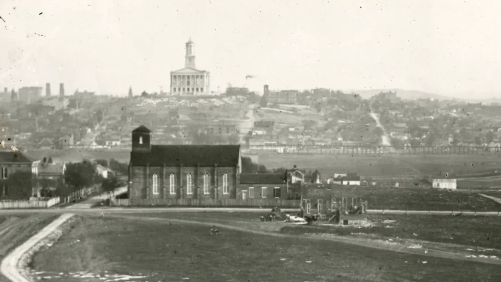 Historic black and white cityscape showing Tennessee State Capitol atop hill with church in foreground view