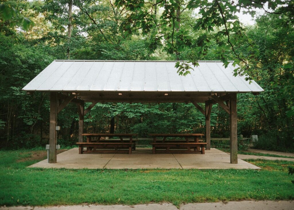Handcrafted wooden picnic structure at Warner Park, with wooden roof and sitting benches in natural setting.