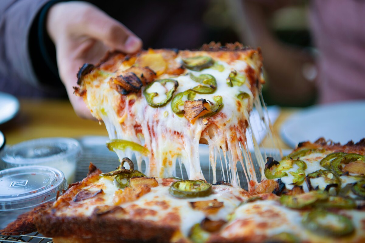 Cheesy jalapeño pizza slice from one of the best East Nashville restaurants being lifted with melted mozzarella stretching down