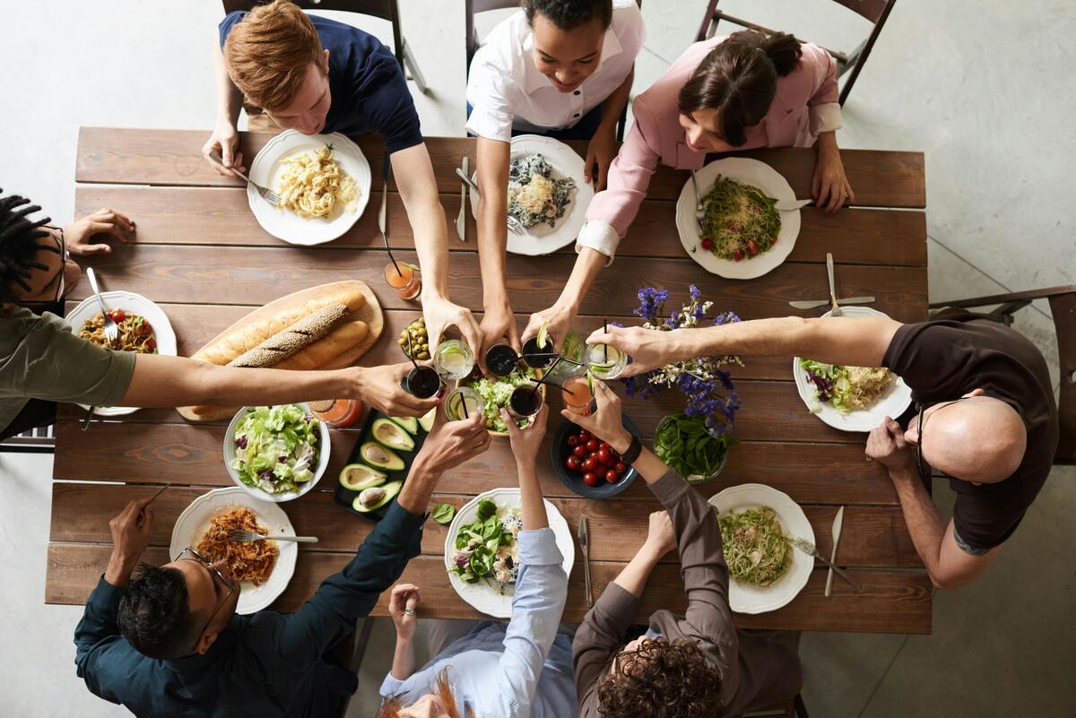 Family enjoys a communal dinner party, sharing food and drinks around a rustic wooden table together.