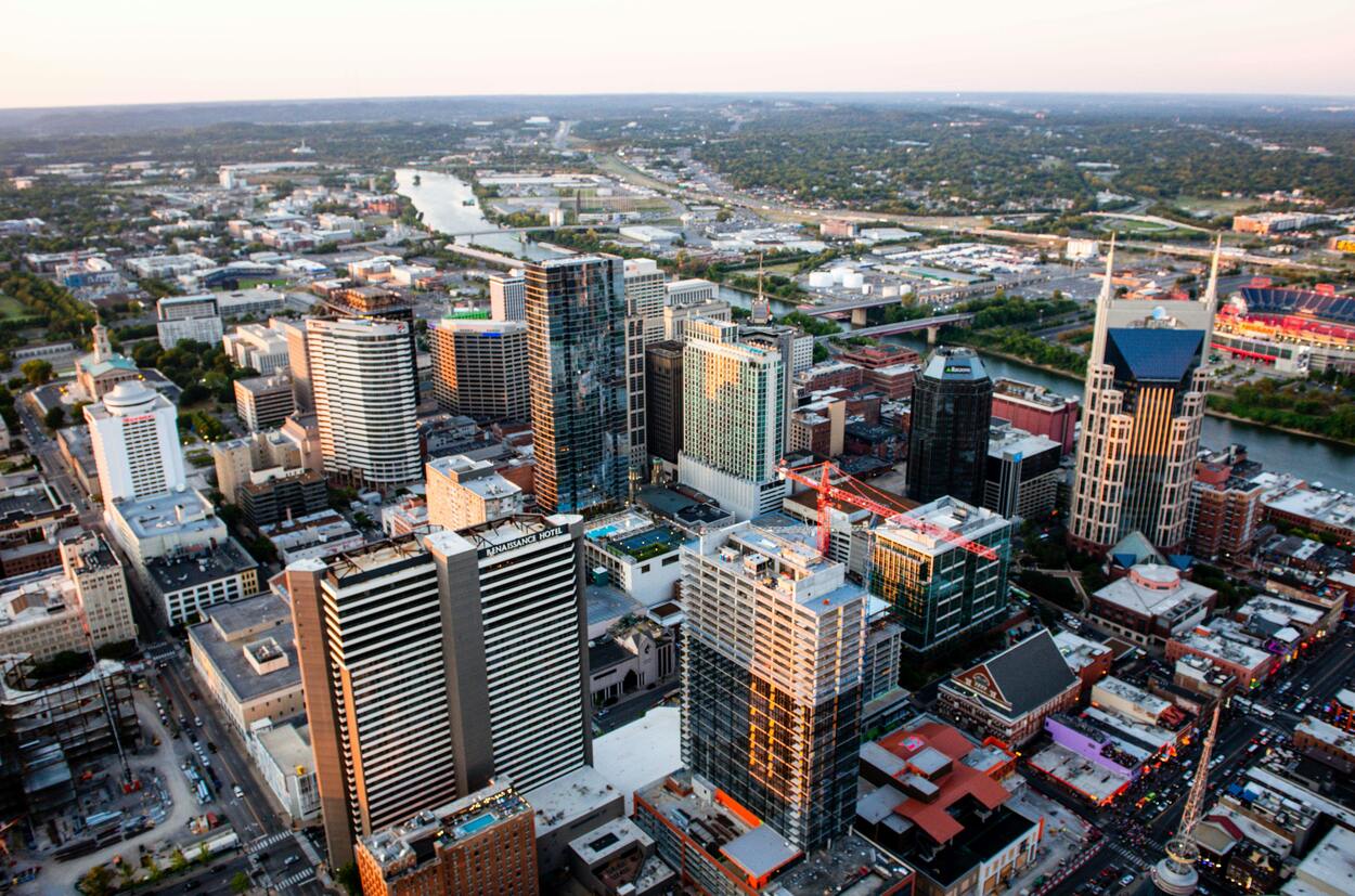 An aerial view of Nashville’s skyline shows modern high-rises, the winding Cumberland River, and urban sprawl at golden hour