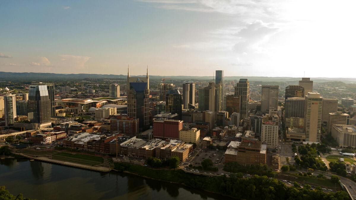 Nashville skyline at sunset, dense urban core with skyscrapers along Cumberland River, surrounded by rolling hills