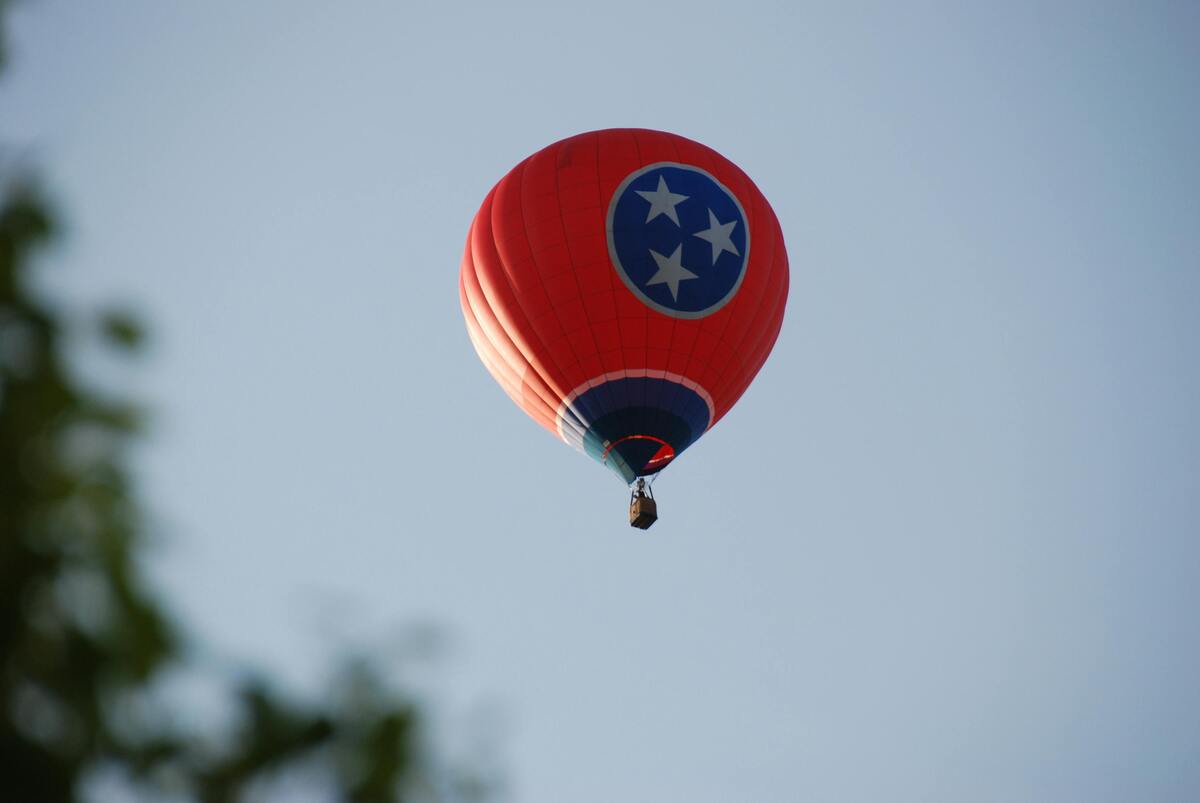 Tennessee Facts hot air balloon with state flag design floating in clear blue sky above treetops