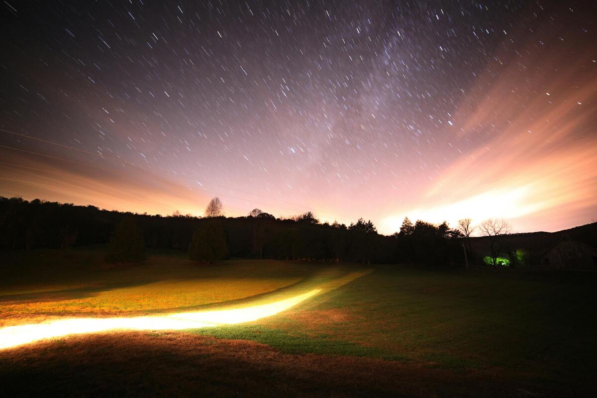 Tennessee Facts starry night sky with light trails over rural landscape and distant tree line silhouette